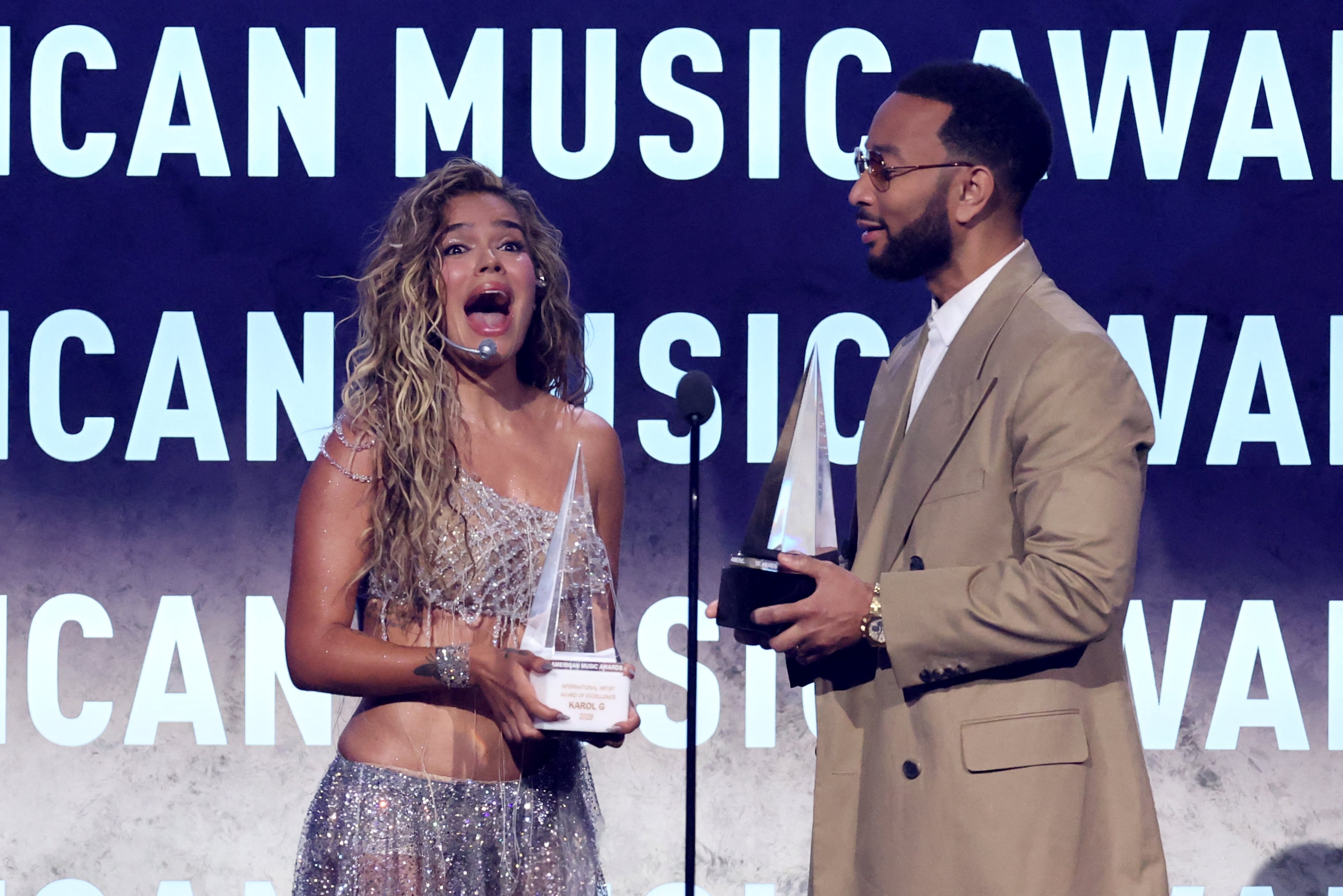 La cantante colombiana Karol G recibe de John Legend el Premio Internacional a la Excelencia Artística y el de Mejor Álbum Latino por “Tropicoqueta” durante los American Music Awards 2026 en Las Vegas.
