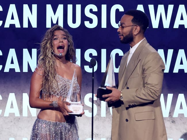 La cantante colombiana Karol G recibe de John Legend el Premio Internacional a la Excelencia Artística y el de Mejor Álbum Latino por “Tropicoqueta” durante los American Music Awards 2026 en Las Vegas.
