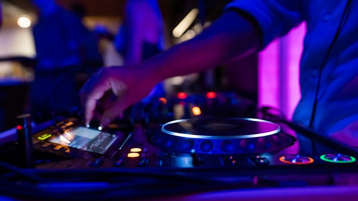A DJ on a party mixing, controlling the volume and making music on stage with DJ equipment during the night in a colourful setting