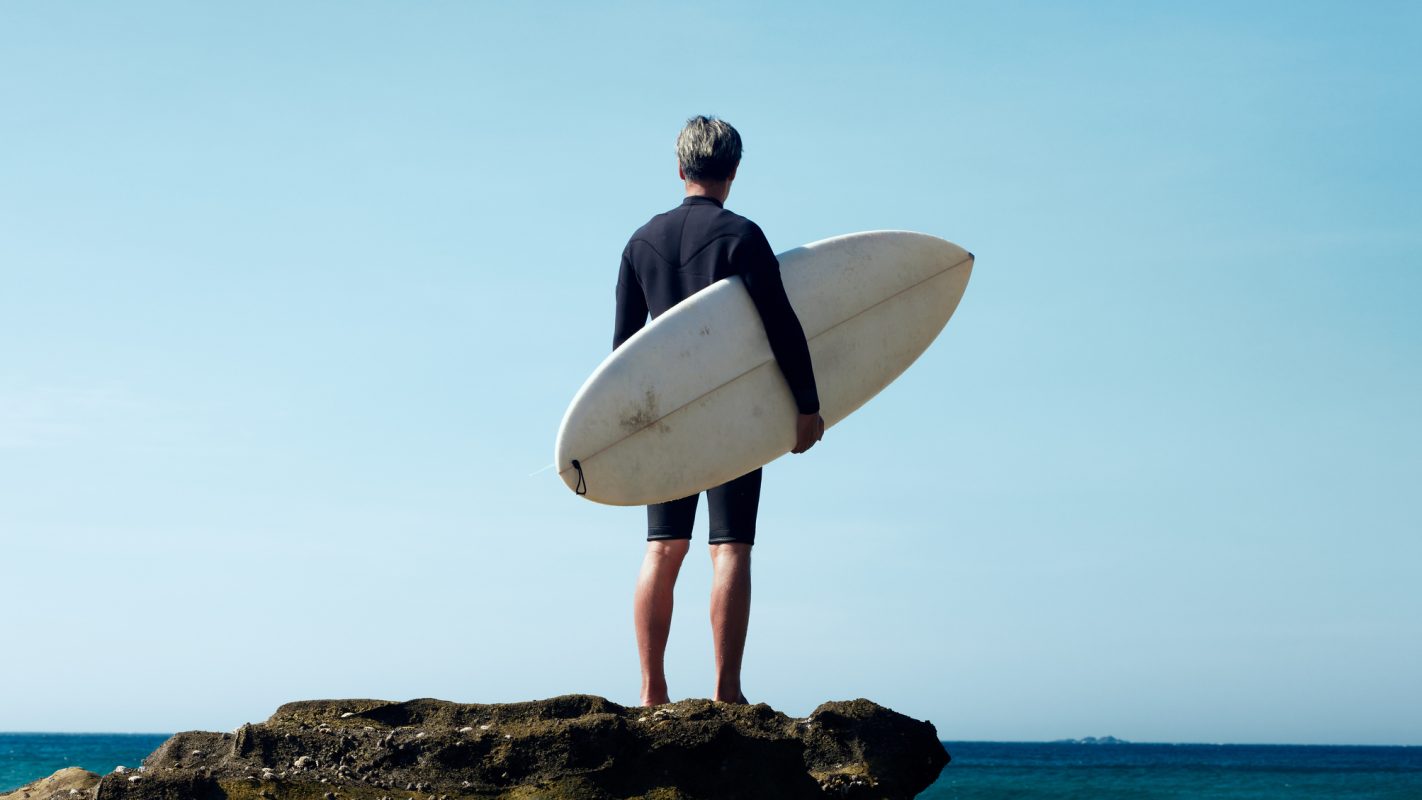 Portrait of a man standing with his surfboard in front of the wind and waves.
