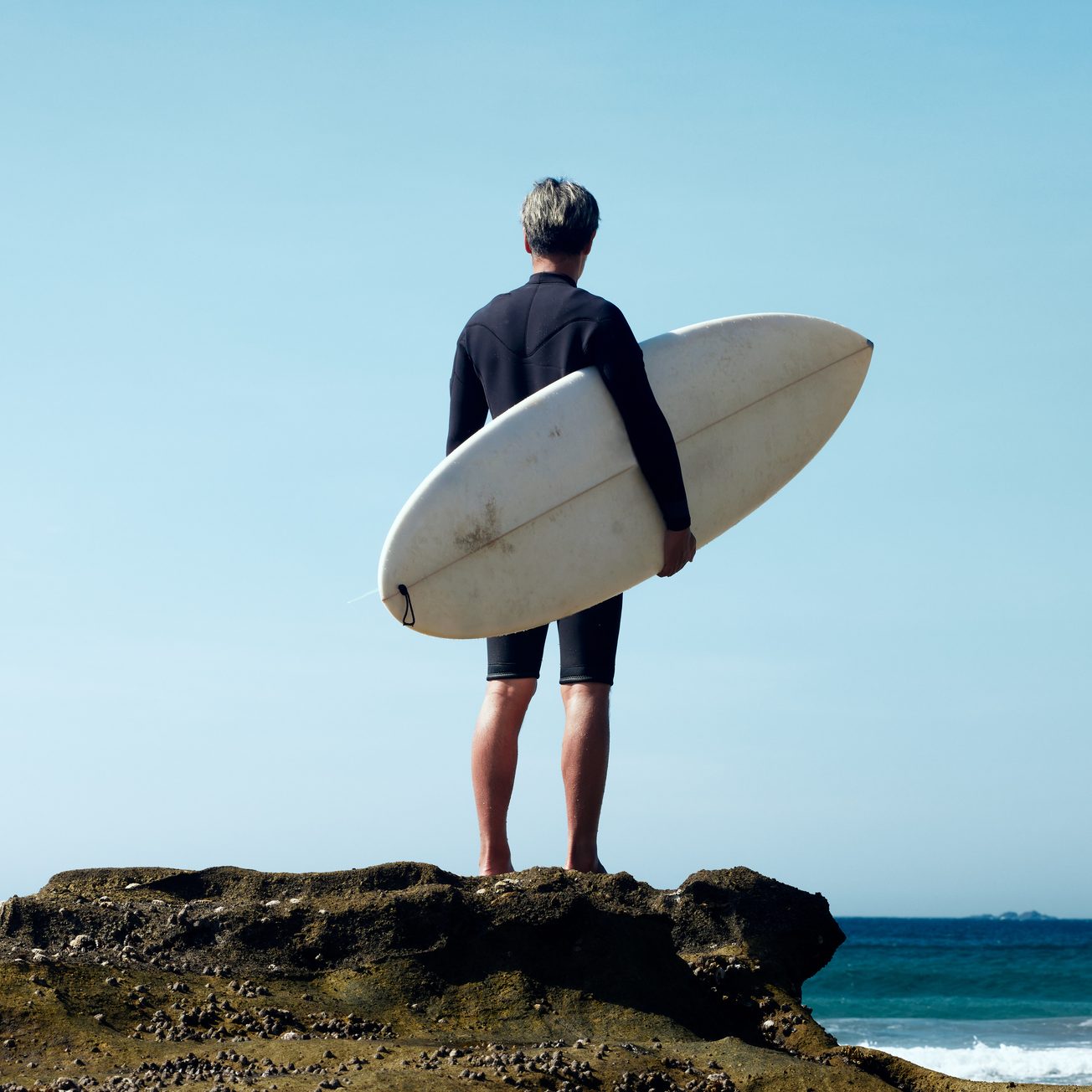 Portrait of a man standing with his surfboard in front of the wind and waves.
