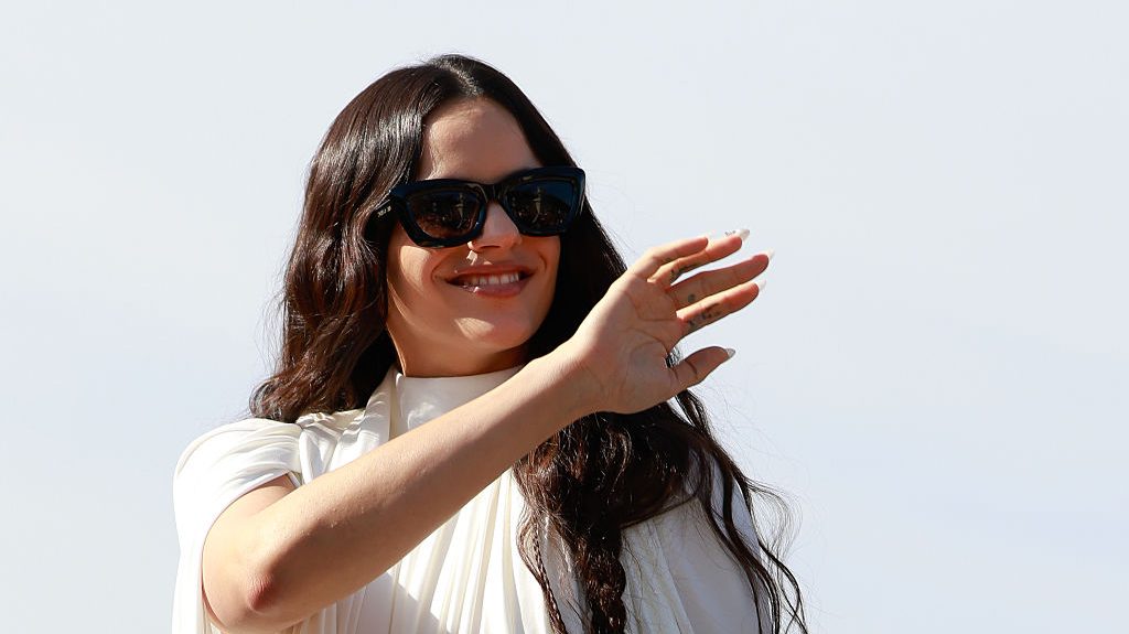 Rosalía con un vestido corto de gasa blanca de cuello alto, zapatos con lazo negros y gafas de sol negras de Dior